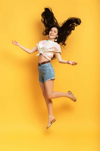 全景快乐的黑发女孩跳在黄色背景上 — 图库照片