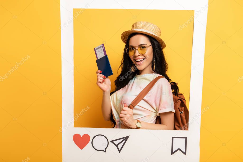happy brunette girl in summer outfit holding air ticket in social network frame on yellow background