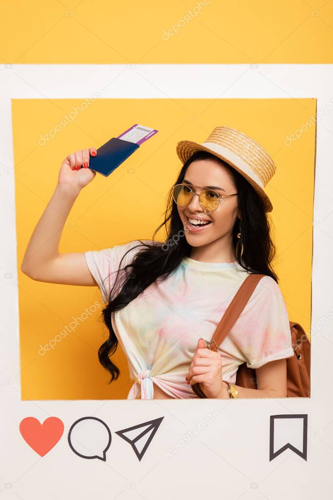 happy brunette girl in summer outfit holding air ticket in social network frame on yellow background