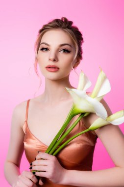 Zarif sarışın kadın pembeye izole edilmiş kalla çiçekleri tutuyor.