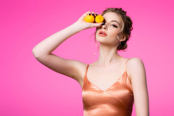 elegant beautiful blonde woman in silk dress holding apricots isolated on pink