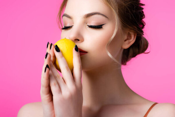 beautiful blonde woman smelling ripe lemon isolated on pink