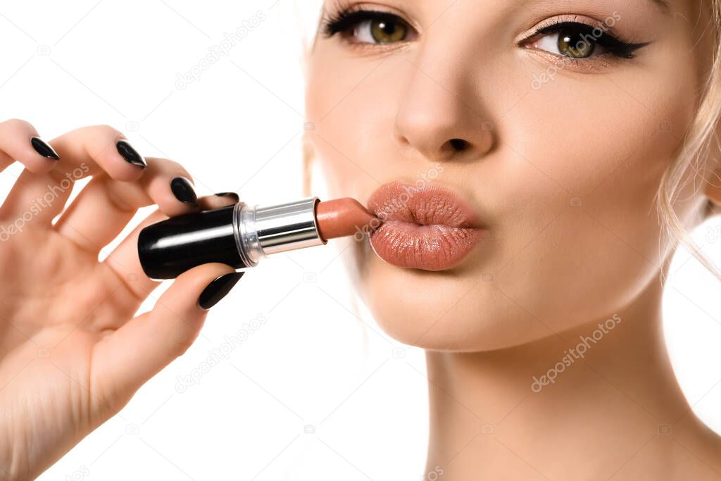 close up view of beautiful woman holding beige lipstick near lips isolated on white