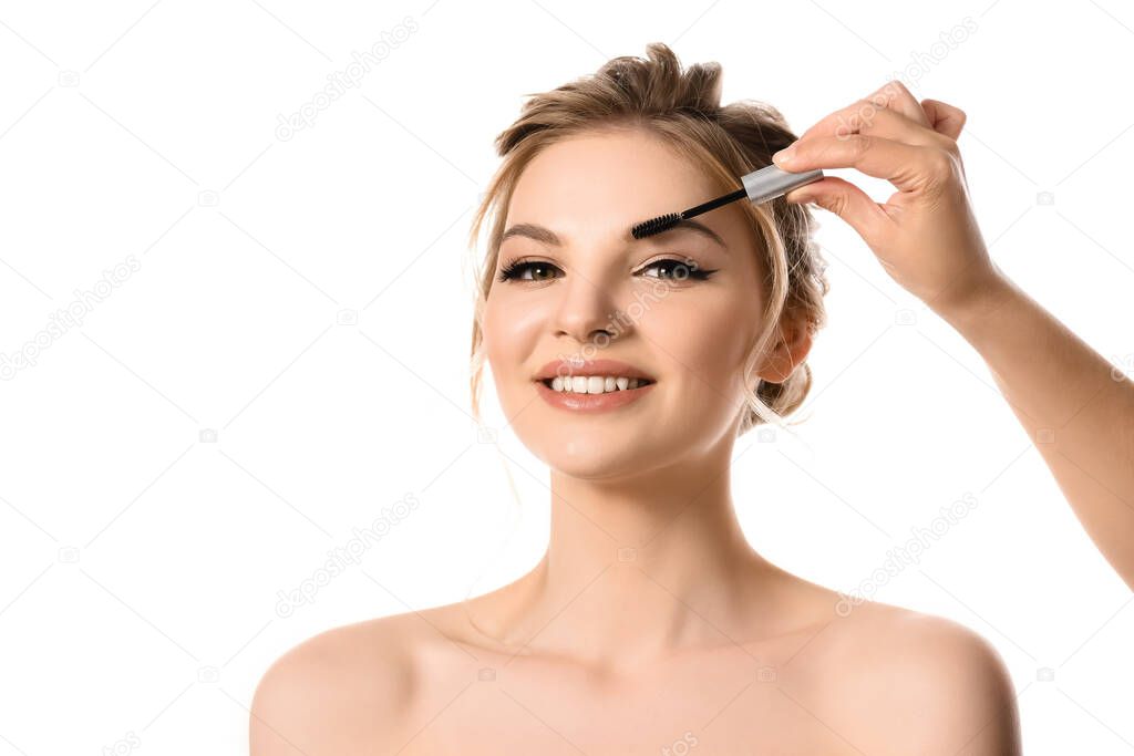 hand with brow mascara near smiling naked beautiful blonde woman isolated on white