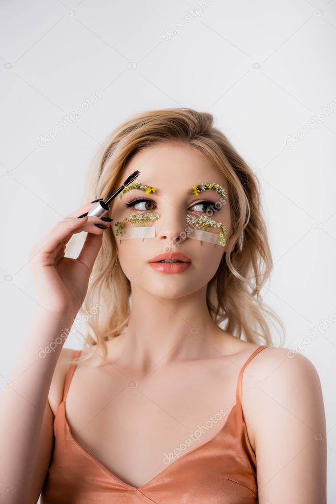beautiful blonde woman in silk dress with wildflowers on eyebrows and brow gel isolated on white
