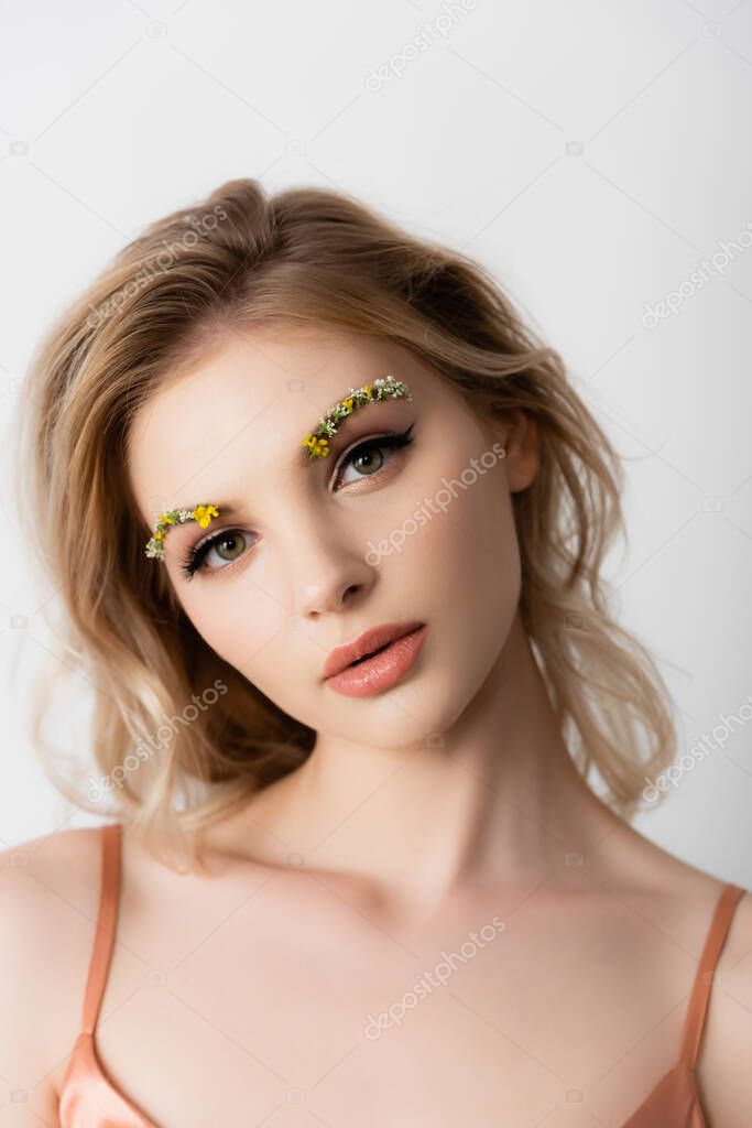 beautiful blonde woman with wildflowers on eyebrows looking at camera isolated on white