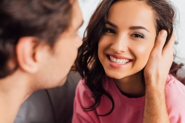 Seçici odak noktası, erkeğin kameraya gülümseyen güzel bir kadına dokunması gri koltukta izole edilmiş. 