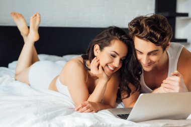 Evde dizüstü bilgisayar kullanan genç pozitif çiftin seçici odak noktası 