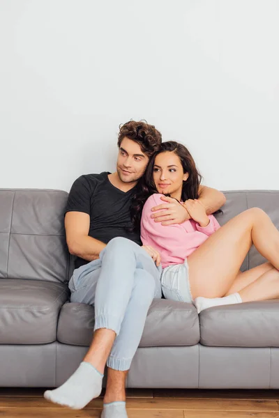英俊潇洒的男人在家里沙发上拥抱美丽的女朋友的选择性焦点 — 图库照片