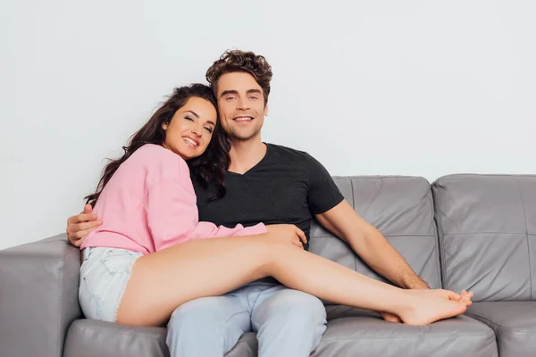 Young Man Hugging Girlfriend Smiling Camera Couch Isolated Grey — Stock Photo, Image