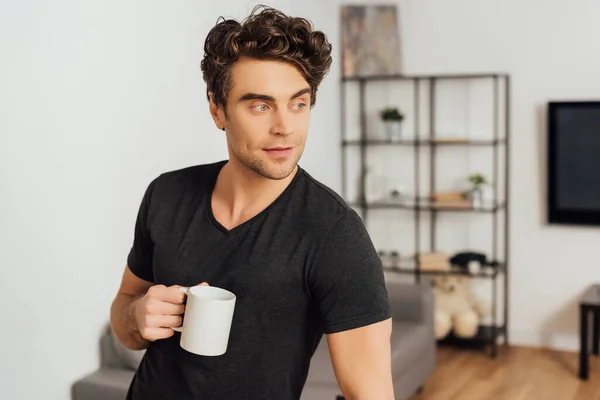 Schöner Mann Hält Tasse Kaffee Der Hand Und Schaut Wohnzimmer — Stockfoto