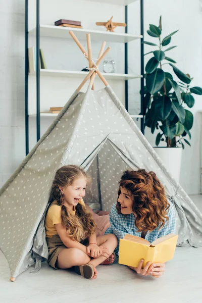 Lächelnder Babysitter Schaut Lachendes Kind Während Buch Kinderwigwam Hält — Stockfoto