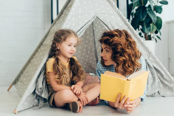 Genç Bebek Bakıcısı Oyun Çadırında Kitap Tutarken Sevimli Çocuğa Bakıyor — Stok fotoğraf