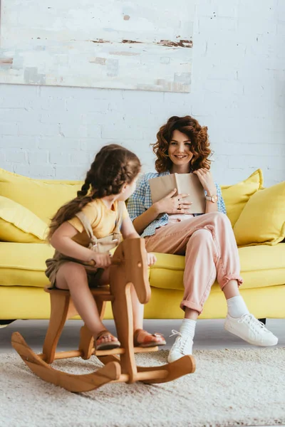 Niñera Sonriente Sentado Sofá Con Libro Mirando Los Niños Caballo —  Fotos de Stock