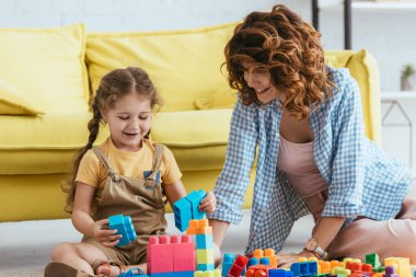Neşeli bebek bakıcısı ve çocuk yerde otururken yapı taşlarıyla oynuyorlar.