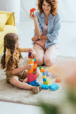 Güler yüzlü bir dadının, çocuğun yanında otururken yerde birlikte oynamalarının seçici odağı