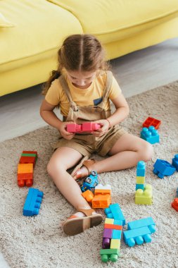 high angle view of kid sitting on floor and playing with multicolored building blocks clipart