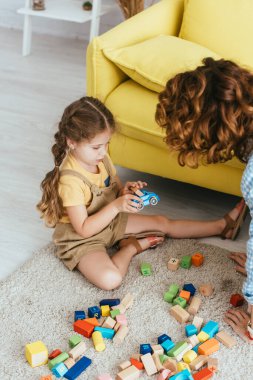 Dadı ve renkli blokların yanında yerde otururken oyuncak araba tutan sevimli çocuğun yüksek açılı görüntüsü