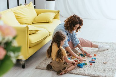 Genç dadı ve çocuğun seçici odak noktası yerde oturup çok renkli bloklarla oynamak.