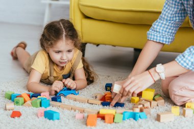 partial view of babysitter and kid playing with multicolored blocks of floor clipart