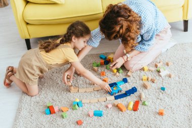 high angle view of babysitter and kid playing with multicolored blocks and toy car on floor clipart