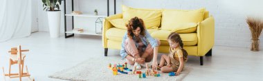 horizontal image of nanny and kid playing with multicolored blocks on floor clipart