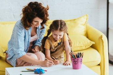 young babysitter and adorable kid drawing with pencils together clipart