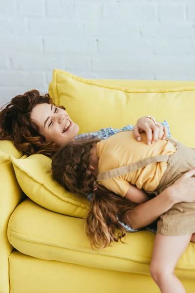 Stock image child lying on laughing nanny while having fun on sofa at home