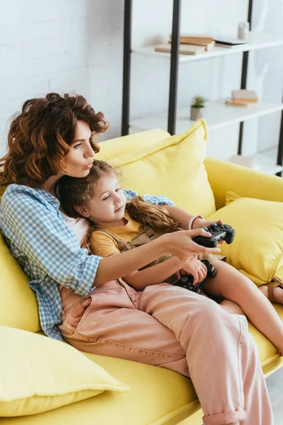 集中保姆和小孩坐在黄色沙发上玩电子游戏 — 图库照片