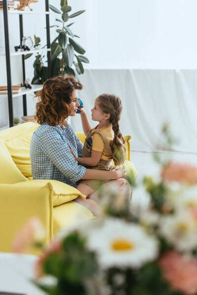 избирательный фокус очаровательного ребенка, сидящего на коленях молодой няни, глядя друг на друга