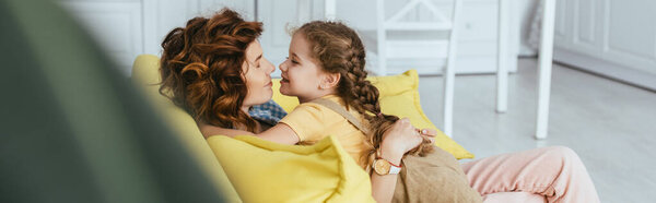 selective focus of adorable child hugging happy nanny sitting on sofa, panoramic crop