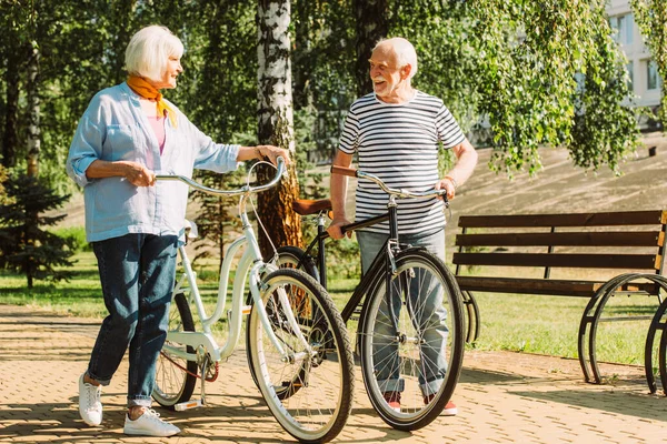 Casal Idosos Sorrindo Para Outro Enquanto Caminham Com Bicicletas Parque — Fotografia de Stock