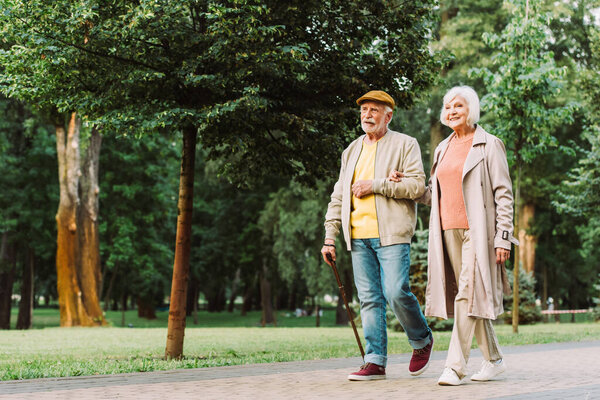Улыбающаяся пожилая женщина, идущая рядом с мужем по дорожке в парке 