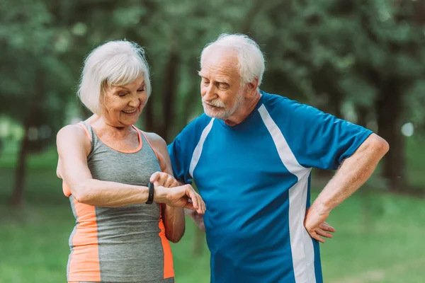 Glimlachende Senior Vrouw Zoek Naar Fitness Tracker Buurt Van Echtgenoot — Stockfoto