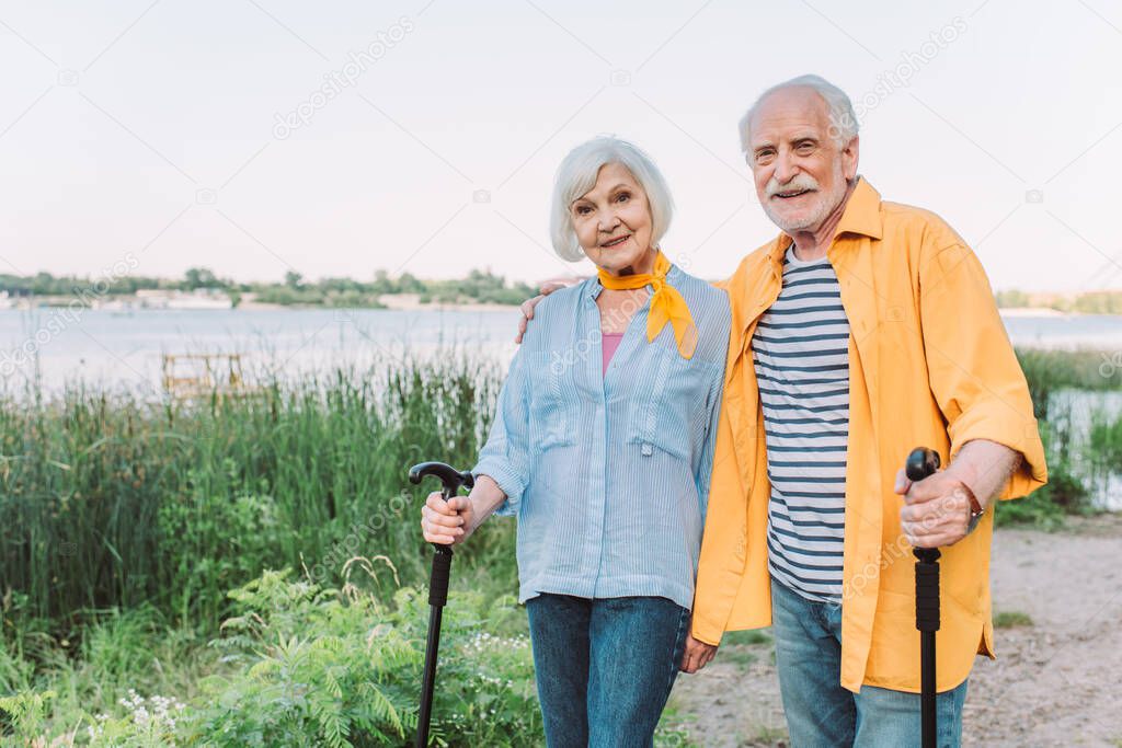Smiling senior man embracing wife with walking stick in park 
