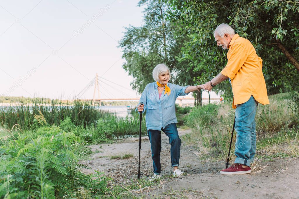 Smiling senior man helping wife with walking stick on path in park 