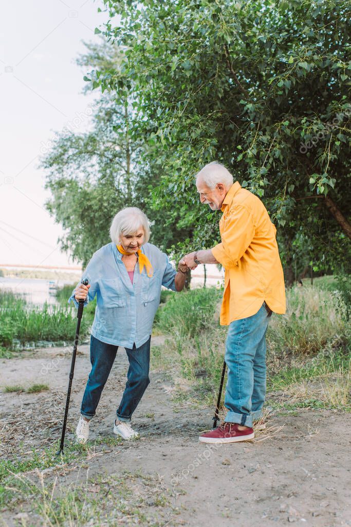 Senior man helping wife with walking stick on pathway in park 