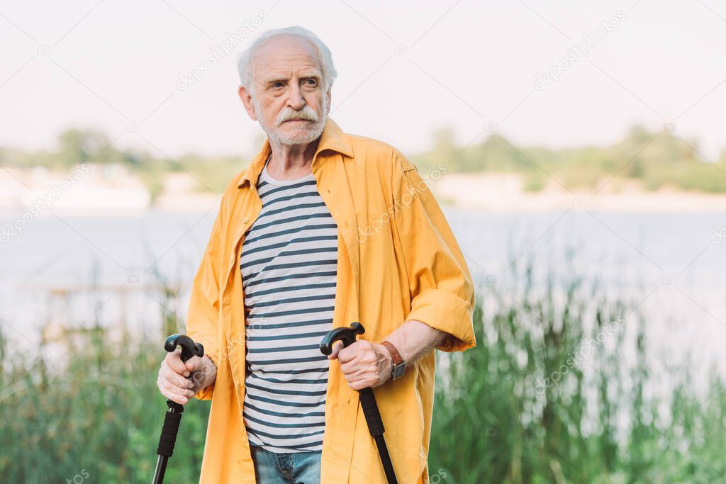 Senior man holding walking sticks while looking away in park 