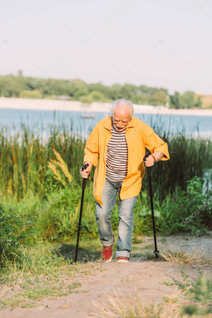 Selective focus of senior man with walking sticks walking on path in park 