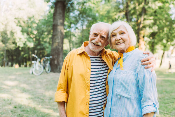 Positive senior man hugging smiling wife in summer park 