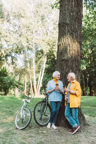 Älteres Paar Lächelt Sich Während Pappbecher Neben Baum Und Fahrrädern — Stockfoto