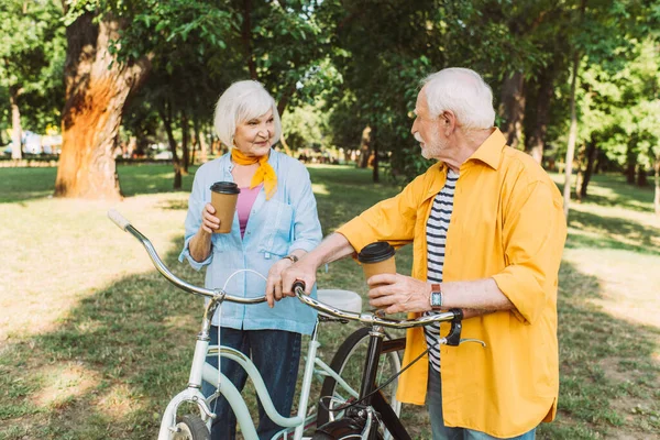 Smiling senior couple with coffee to go and bikes in park