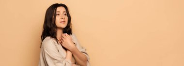 Web sitesi başlığı: Bej rengi göğüslerin yanında sıkıca tutarken bakışlarını kaçıran endişeli kadın