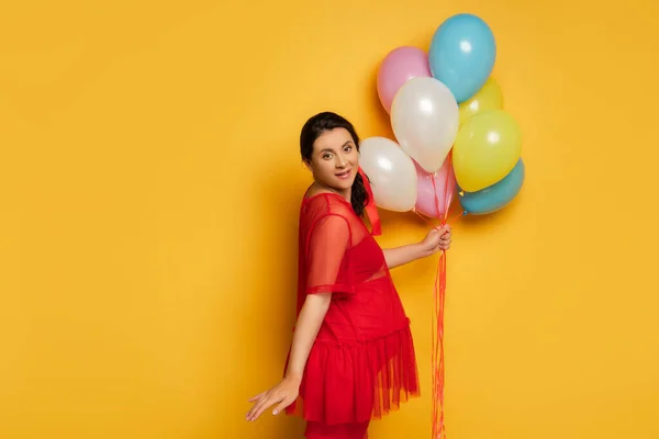 Zwanger Vrouw Rode Tuniek Houden Kleurrijke Feestelijke Ballonnen Terwijl Kijken — Stockfoto