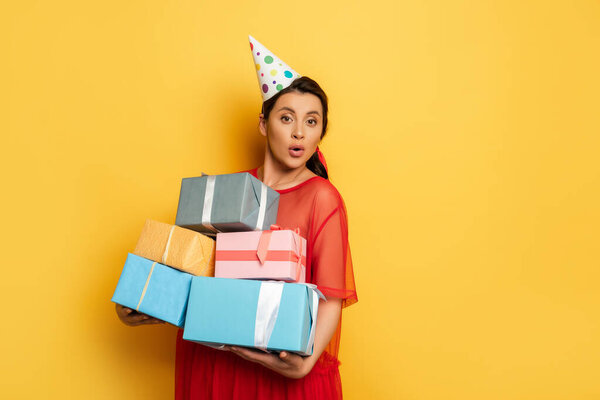 pregnant woman in party car holding stack of gift boxes while looking at camera on yellow
