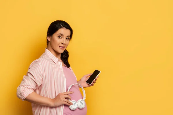 Έγκυος Γυναίκα Smartphone Κρατώντας Ασύρματα Ακουστικά Κοντά Στην Κοιλιά Κίτρινο — Φωτογραφία Αρχείου
