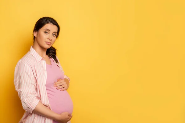 Молодая Беременная Женщина Смотрит Камеру Прикасаясь Желтому Животу — стоковое фото