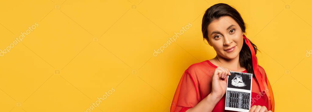 Panoramic crop of pregnant woman in red tunic holding ultrasound scan on yellow