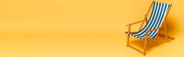 Sarı zemin üzerinde çizgili mavi ve beyaz güverte sandalyesinin yatay görüntüsü