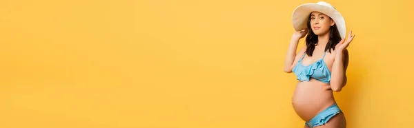 Panoramiczne Ujęcie Ciężarnej Kobiety Dotykającej Słomkowego Kapelusza Patrząc Żółty Aparat — Zdjęcie stockowe